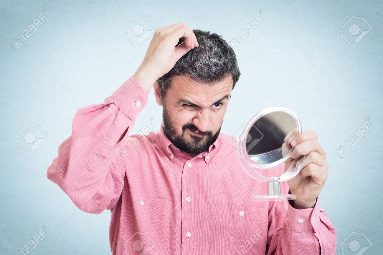 Horrified Young Man Looking In The Mirror At The First Grey Hair
