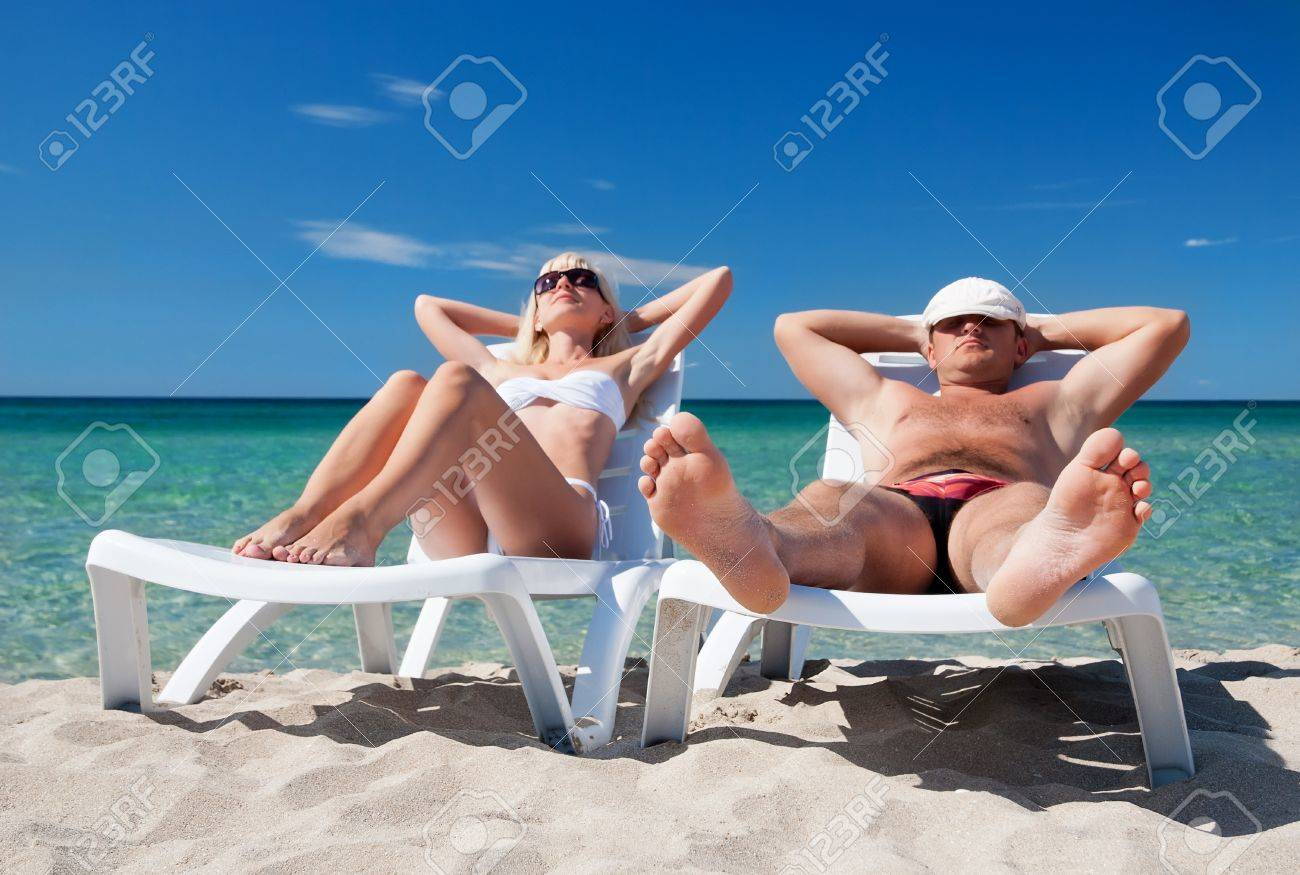 若いカップルが海のビーチでビーチ ベッドで日光浴します の写真素材 画像素材 Image