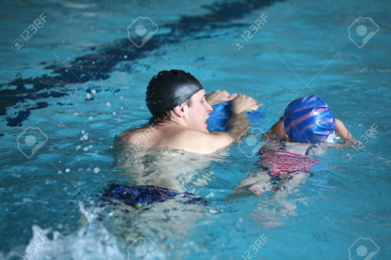 Close up of swimming lesson - child practicing flutter kick with kick board with instructor in indoor swimming pool -back view - 53219794 Close up of swimming lesson - child practicing flutter kick with kick board with instructor in indoor swimming pool -back view - 53219794