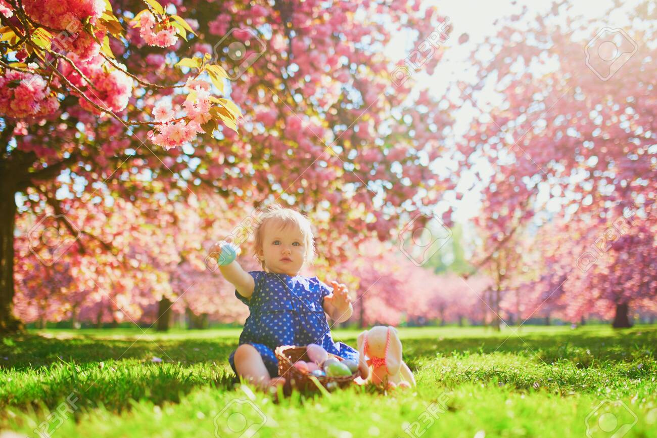 Cute Little One Year Old Girl Playing Egg Hunt On Easter Toddler Sitting On The Grass