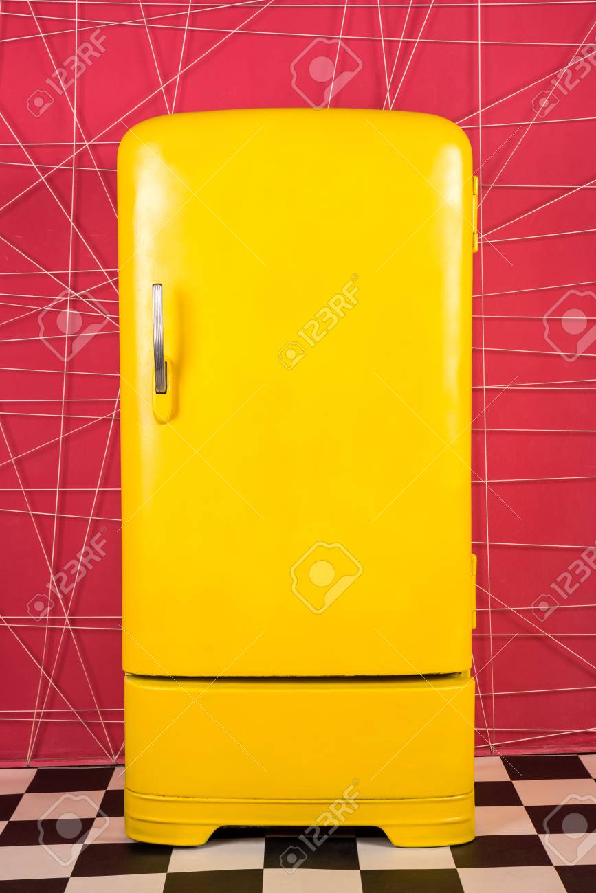 old vintage yellow refrigerator on a pink background