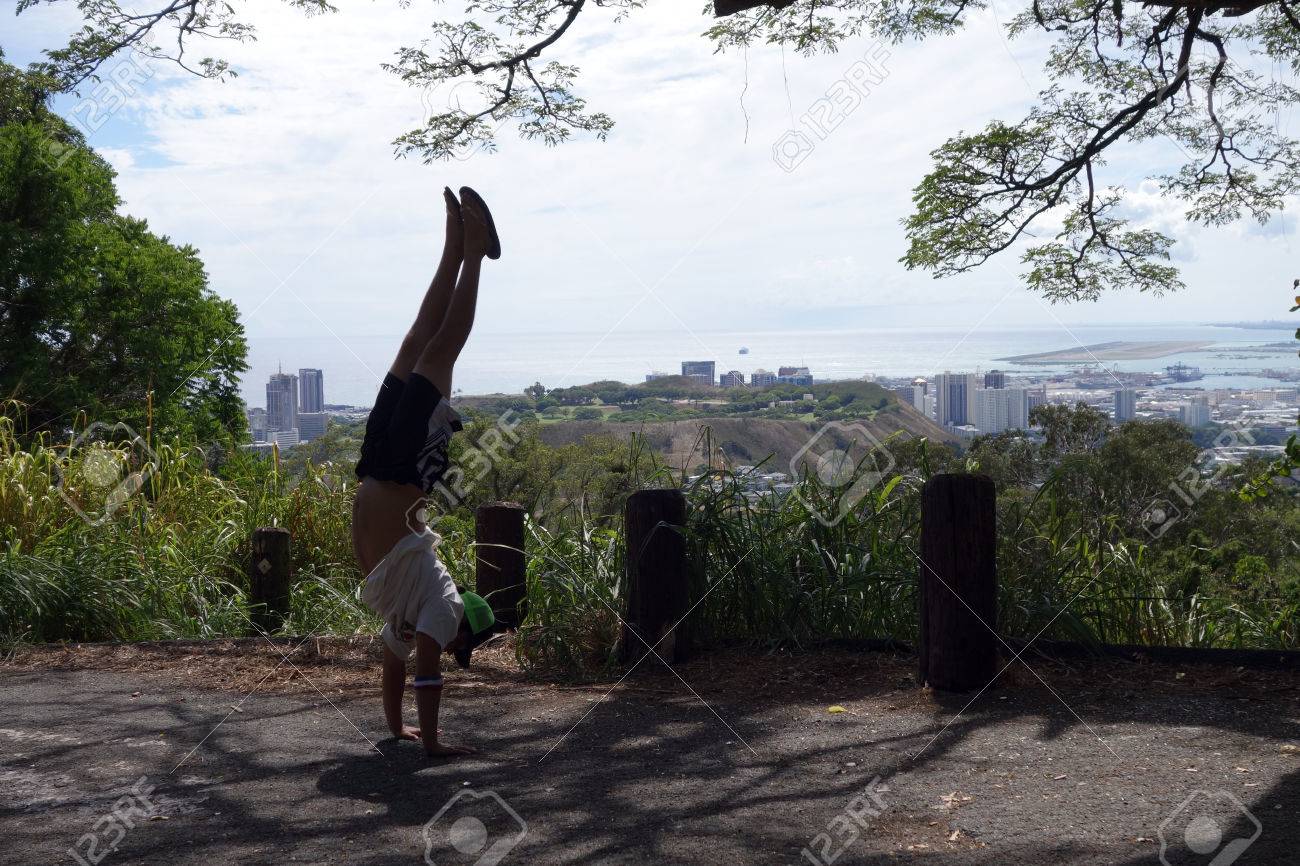 スリッパ逆立ちタンタロス山展望台でバスケット ボール パンツ T シャツ 帽子をかぶっている男 ハワイ オアフ島ビューでパンチボウル ホノルル国際空港を持つホノルル市上ポイントします の写真素材 画像素材 Image