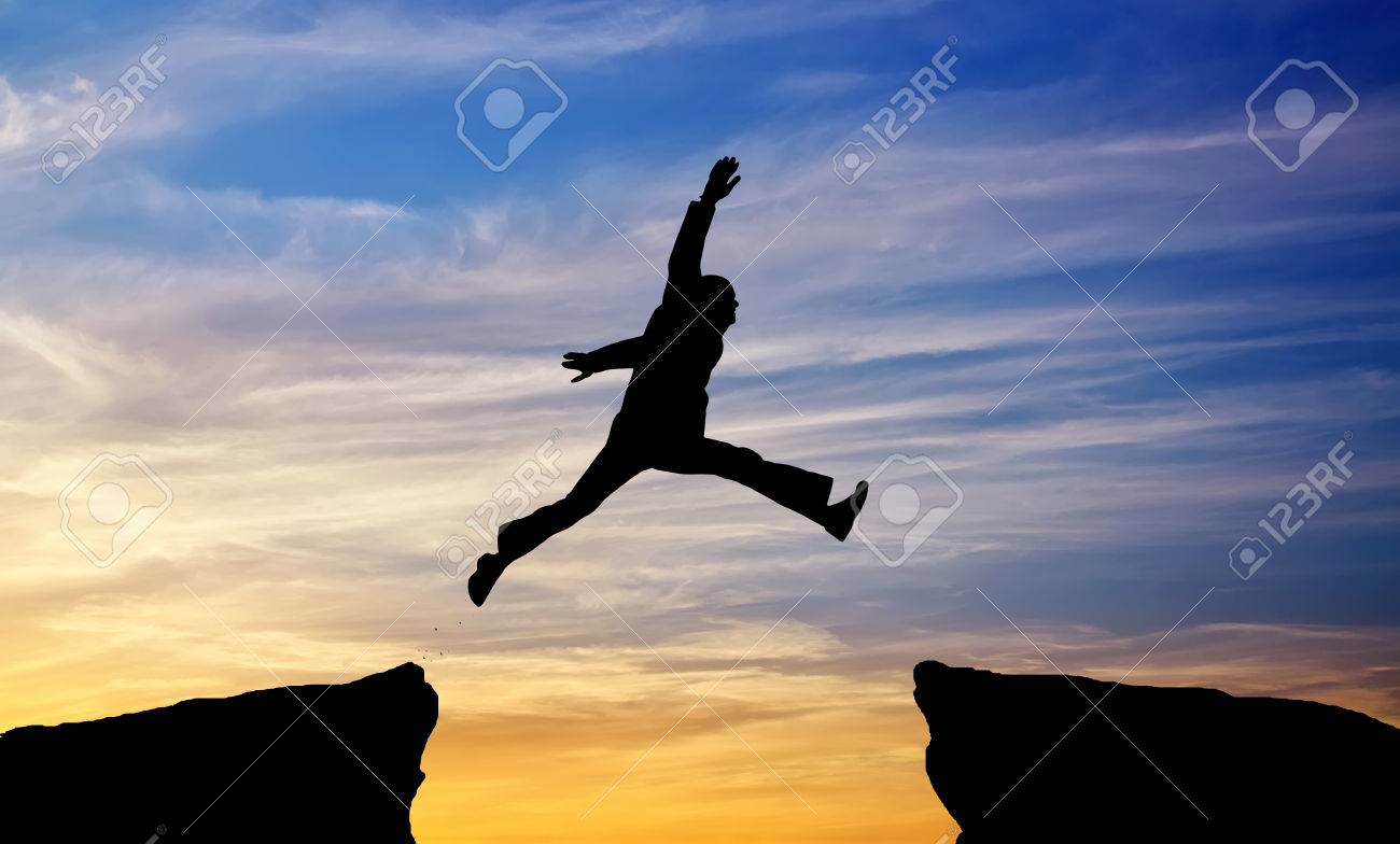 男は燃えるような夕日を背景に隙間からジャンプします の写真素材 画像素材 Image