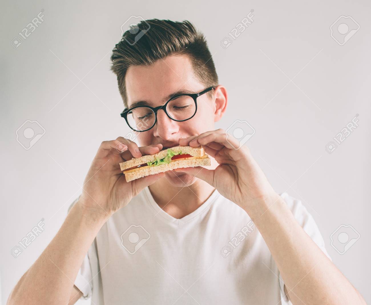 man holding a piece of hamburger. student eats fast food. not helpful food. very hungry man. Nerd is wearing glasses. - 93545034 man holding a piece of hamburger. student eats fast food. not helpful food. very hungry man. Nerd is wearing glasses. - 93545034