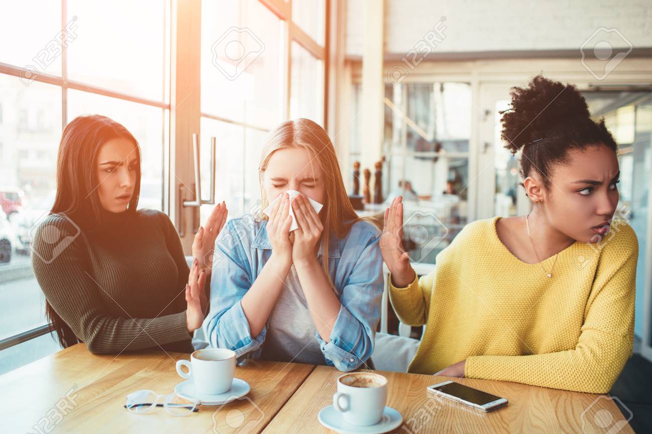 Terrible situation where one girl is sneezing between two of her friends but her friends dont like it. - 96057785 Terrible situation where one girl is sneezing between two of her friends but her friends dont like it. - 96057785