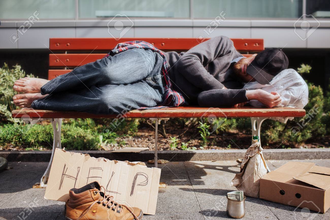 102133611-homeless-man-is-lying-on-bench-and-sleeping-hee-is-tired-and-exhausted-there-is-a-bag-with-stuff-und.jpg