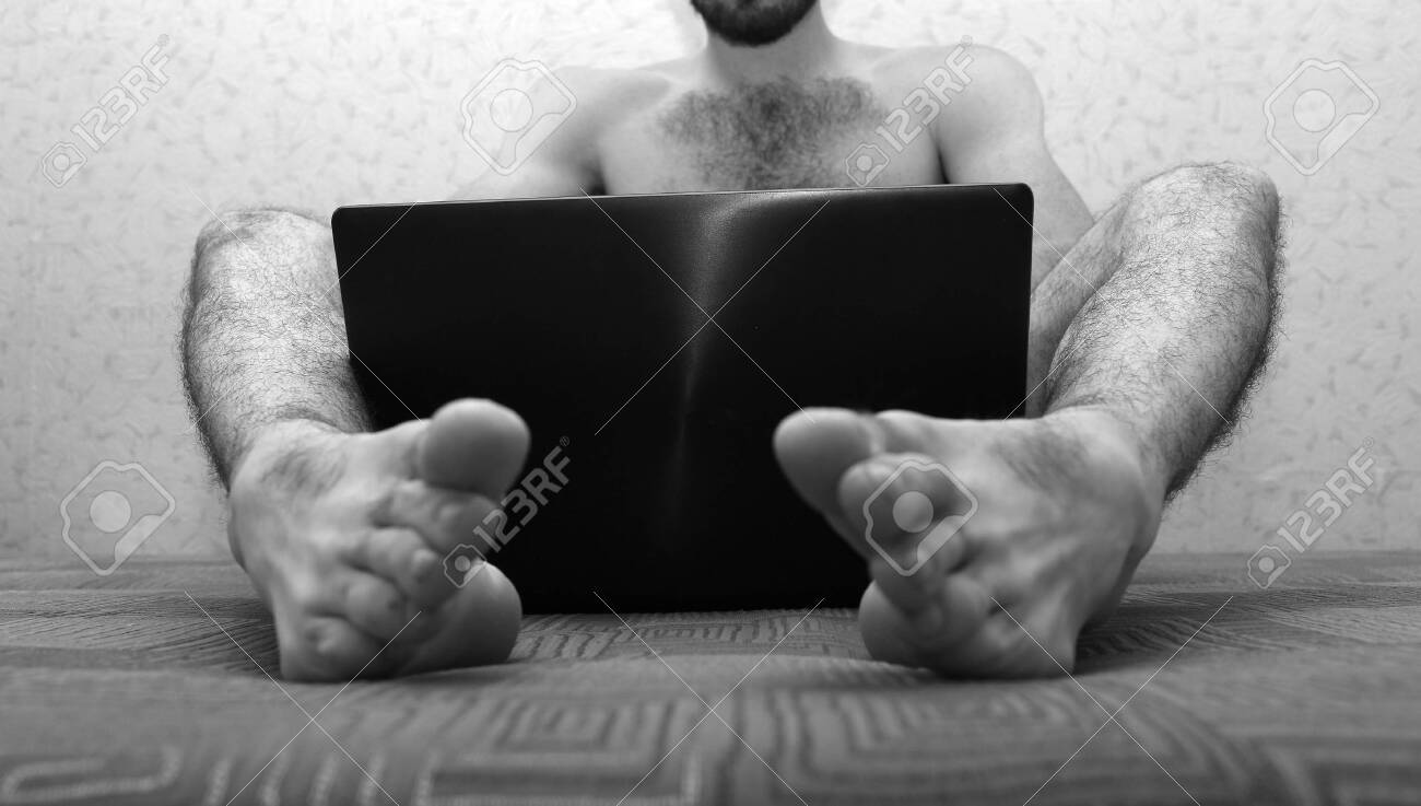 Picture Of Young Naked Man With Hairy Legs Sit On Sofa And Hold Laptop  Between Feet. Cover Himself With Device Screen. Low View. Black And White  Picture. Cut View. Stock Photo, Picture