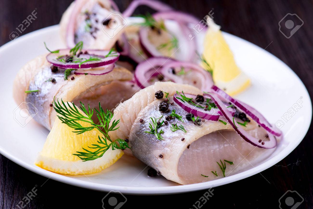 Herring with pepper, herbs, salt and lemon on white ceramic plate on black background - 54798907 Herring with pepper, herbs, salt and lemon on white ceramic plate on black background - 54798907