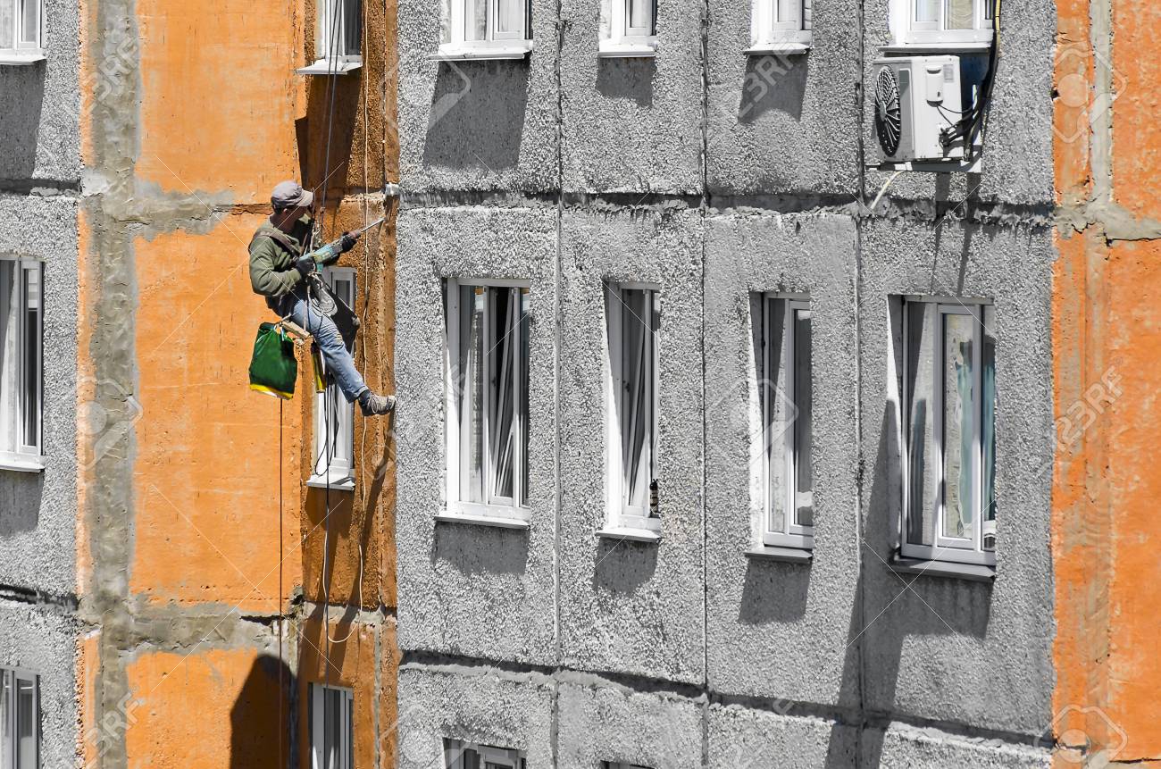 Maintenance Of Joints Between Precast Concrete Panels To Prevent Leakage Through The Wall Worker Climber Hanging On Ropes On A High Rise Building Facade And Cleaning Joints With Hammer Drill Stock Photo Picture
