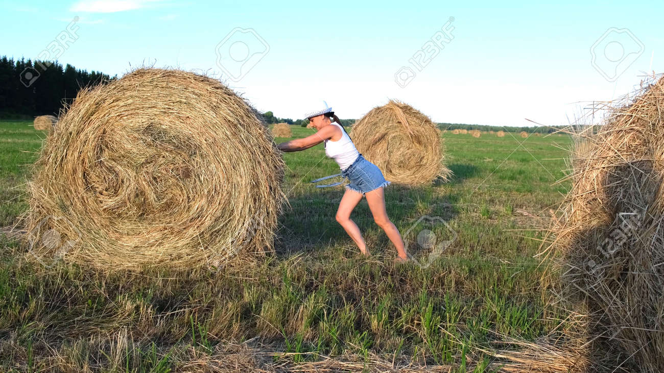 beautiful young girl in a hat pushes a haystack. Rural area. Feminist strong woman concept. - 171399569 beautiful young girl in a hat pushes a haystack. Rural area. Feminist strong woman concept. - 171399569