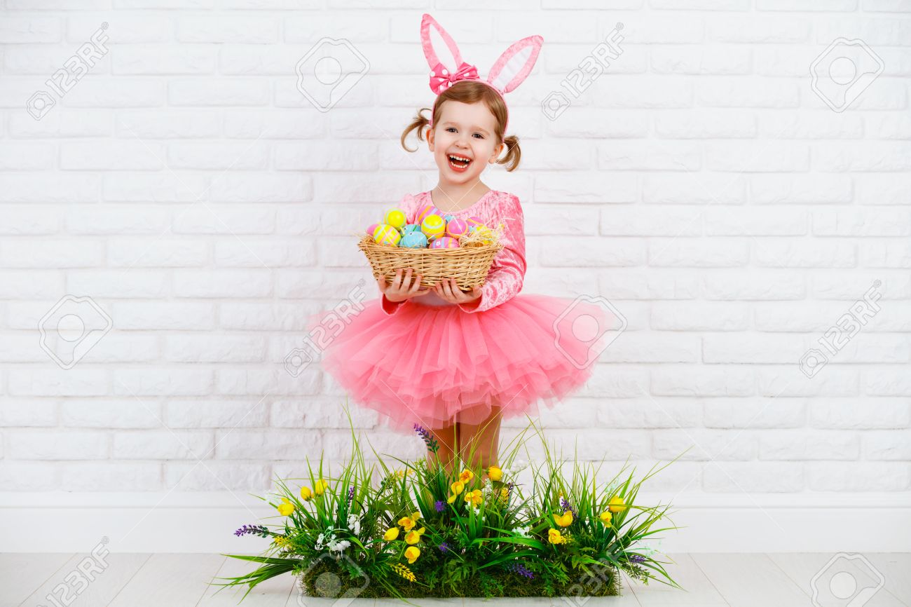 Niña Feliz En Traje Del Conejo De Conejito De Pascua Con Orejas Una Cesta Huevos Y La Hierba Verde Con Las Flores Fotos, Retratos, Imágenes Y Fotografía Archivo