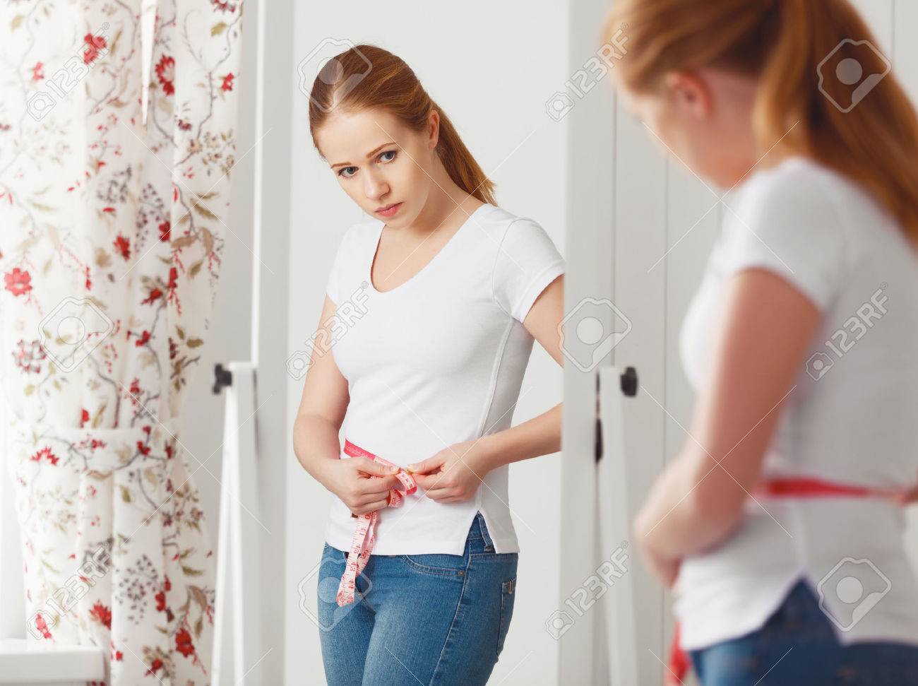 young woman measuring waist with measuring tape in front of a mirror - 61632385 young woman measuring waist with measuring tape in front of a mirror - 61632385
