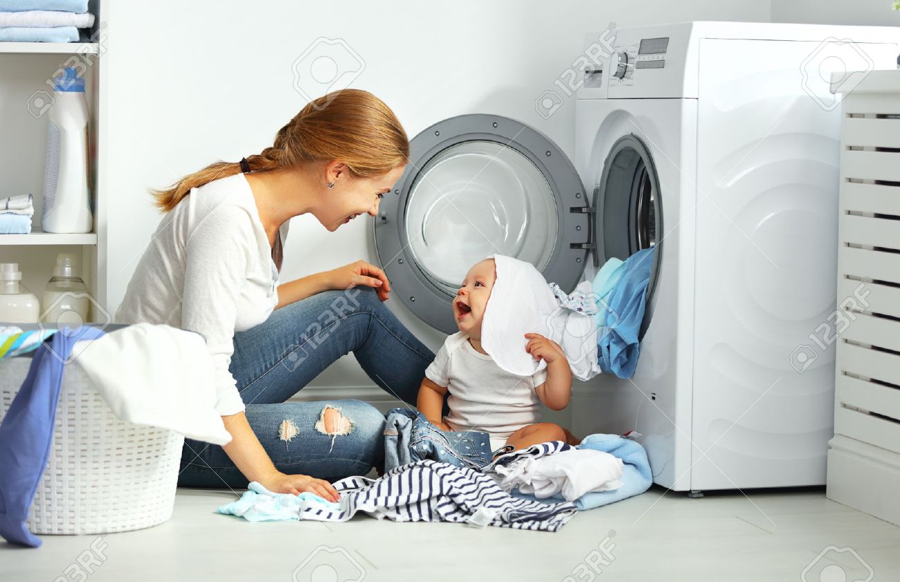 mother a housewife with a baby engaged in laundry fold clothes into the washing machine - 62010003 mother a housewife with a baby engaged in laundry fold clothes into the washing machine - 62010003