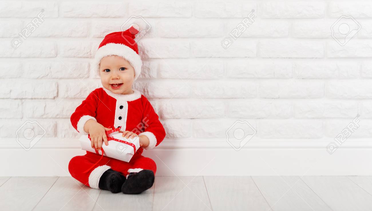 白いレンガの壁にプレゼントとクリスマス コスチューム サンタ クロースで幸せな赤ちゃん の写真素材 画像素材 Image