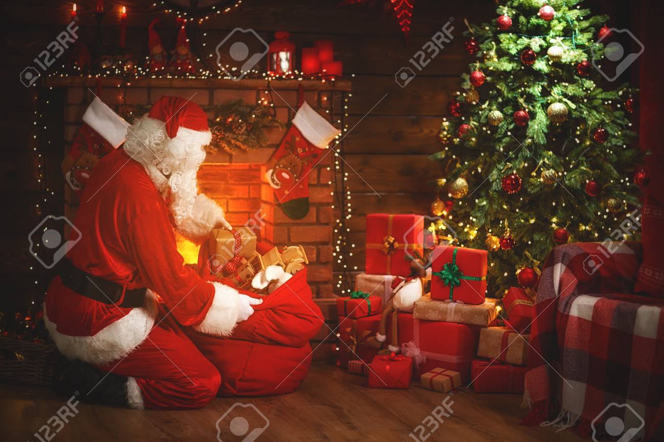 Merry Christmas! Santa Claus Near The Fireplace And Christmas Tree With Gifts Stock Photo, Picture And Royalty Free Image. Image 89727956.