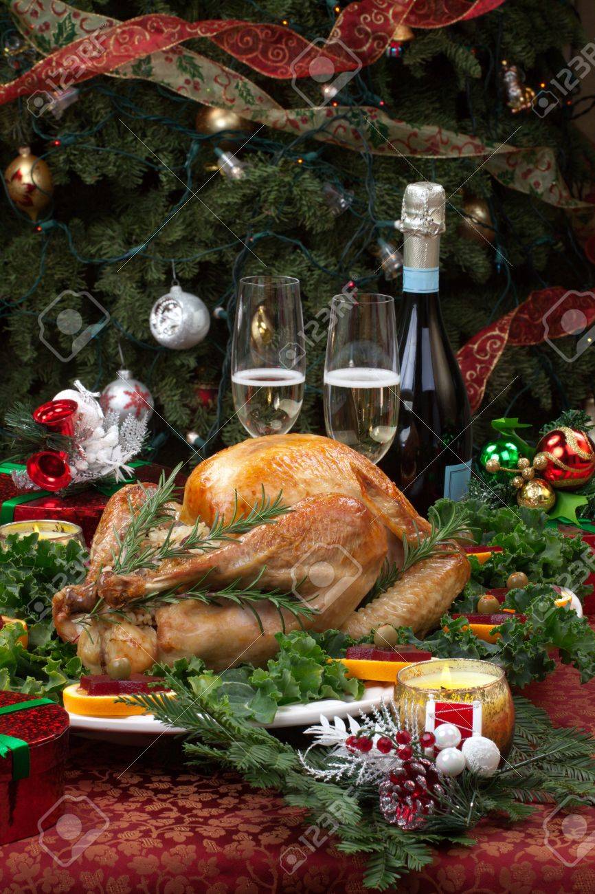 Christmas-decorated table with feast, gifts, roasted turkey, candles, champagne, and Christmas tree on back - 15794120 Christmas-decorated table with feast, gifts, roasted turkey, candles, champagne, and Christmas tree on back - 15794120