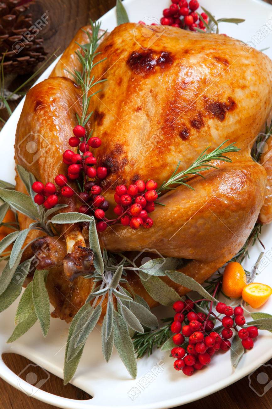 Roasted turkey garnished with sage, rosemary, and red berries in a tray prepared for Christmas dinner. Holiday table, candles and Christmas tree with ornaments. - 32774861 Roasted turkey garnished with sage, rosemary, and red berries in a tray prepared for Christmas dinner. Holiday table, candles and Christmas tree with ornaments. - 32774861