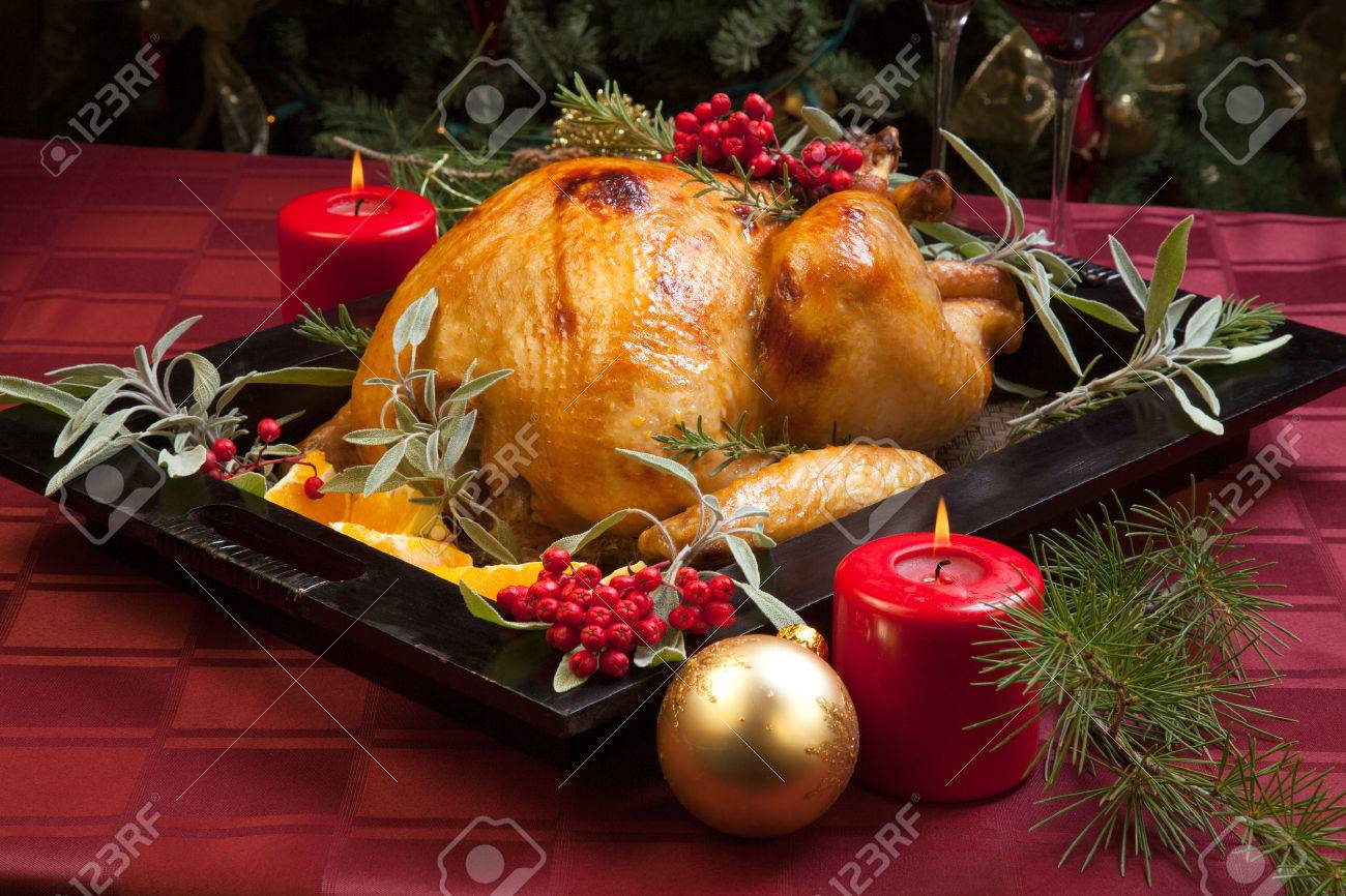 Roasted turkey garnished with sage, rosemary, and red berries in a wooden tray on Christmas decorated table. Candles and Christmas tree with ornaments. - 34609554 Roasted turkey garnished with sage, rosemary, and red berries in a wooden tray on Christmas decorated table. Candles and Christmas tree with ornaments. - 34609554