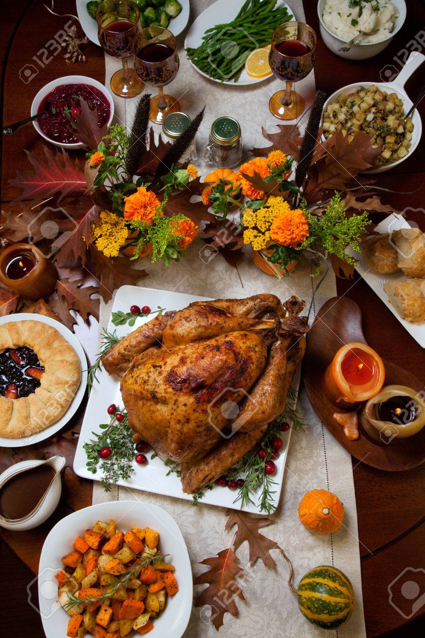Roasted turkey garnished with cranberries on a rustic style table decoraded with pumpkins, gourds, asparagus, brussel sprouts, baked vegetables, pie, flowers, and candles. - 44237212 Roasted turkey garnished with cranberries on a rustic style table decoraded with pumpkins, gourds, asparagus, brussel sprouts, baked vegetables, pie, flowers, and candles. - 44237212