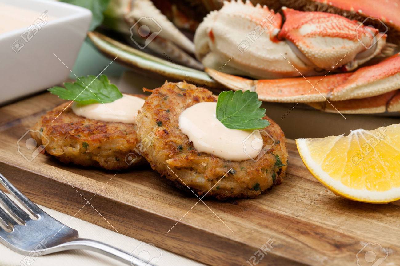 Three crab cakes appetizer with spicy sauce and fresh parsley. Dungeness crab in the background. - 58390544 Three crab cakes appetizer with spicy sauce and fresh parsley. Dungeness crab in the background. - 58390544