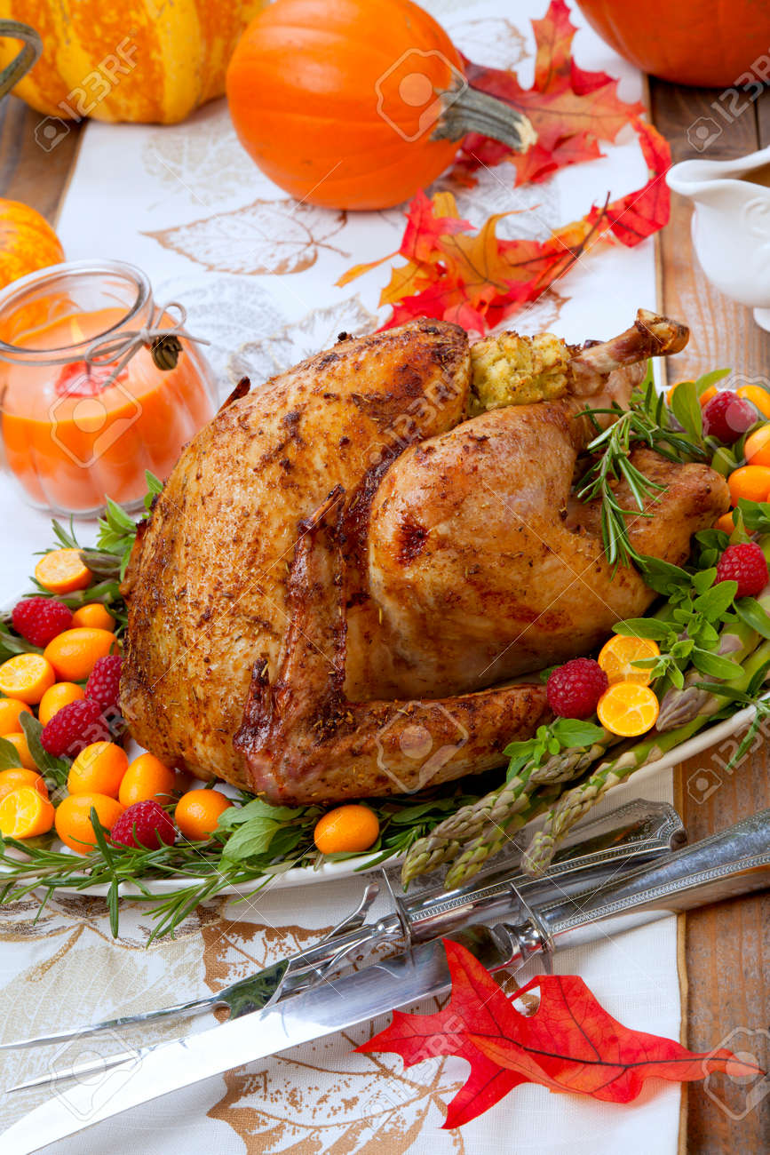 Citrus glazed roasted Turkey for Thanksgiving celebration garnished with kumquat, raspberry, asparagus, oregano, and fresh rosemary twigs. Red wine, side dishes, and gravy. Holiday table decorated with pumpkins, candels, gourds, and fall leaves. - 158534599 Citrus glazed roasted Turkey for Thanksgiving celebration garnished with kumquat, raspberry, asparagus, oregano, and fresh rosemary twigs. Red wine, side dishes, and gravy. Holiday table decorated with pumpkins, candels, gourds, and fall leaves. - 158534599
