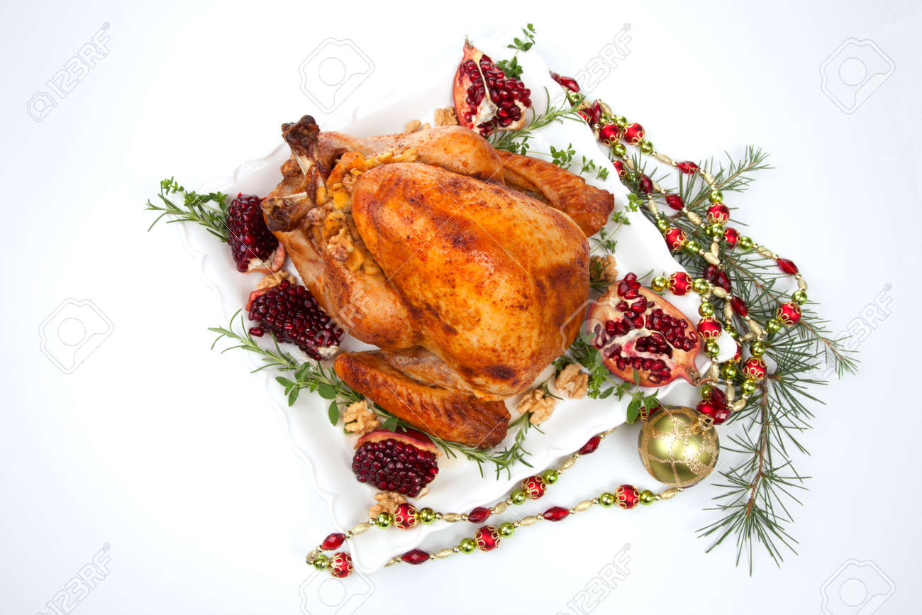 Pomegranate glazed roasted turkey on a tray garnished with fresh pomegranates, herbs, and walnuts over white background. Christmas ornaments and fir twigs. - 159848804 Pomegranate glazed roasted turkey on a tray garnished with fresh pomegranates, herbs, and walnuts over white background. Christmas ornaments and fir twigs. - 159848804
