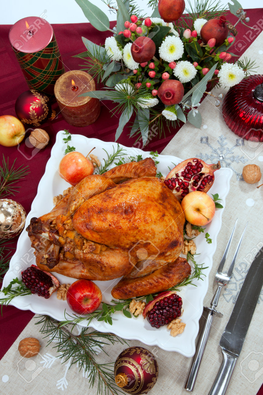 Pomegranate glazed roasted turkey on a tray garnished with fresh pomegranates, apples, herbs, and walnuts on Christmas-decorated table with candles, ornaments, fir twigs and flutes of champagne. - 160495688 Pomegranate glazed roasted turkey on a tray garnished with fresh pomegranates, apples, herbs, and walnuts on Christmas-decorated table with candles, ornaments, fir twigs and flutes of champagne. - 160495688