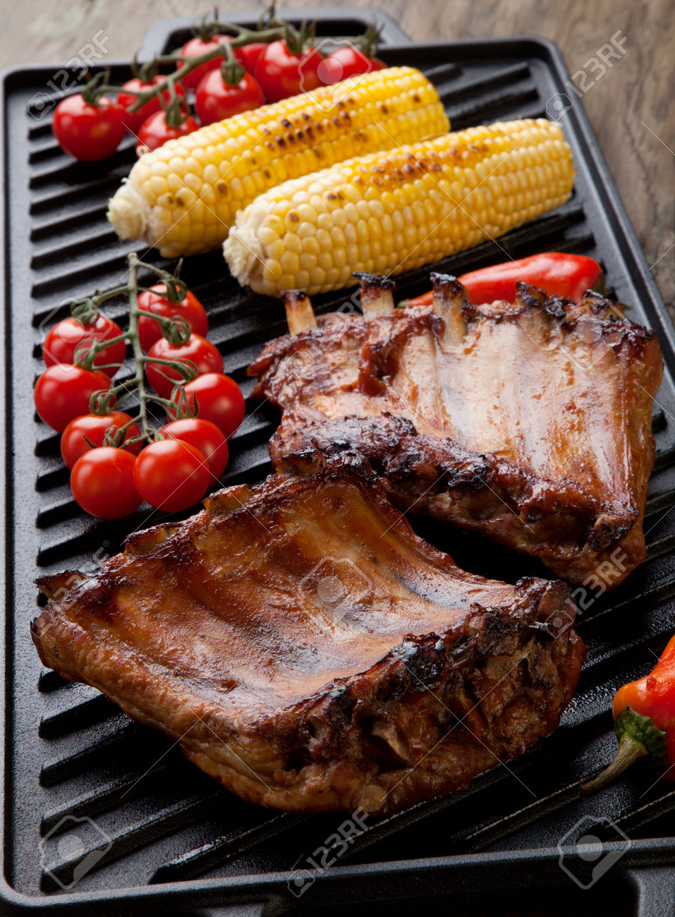 Grilled pork ribs on griddle with chili pepper, cherry tomatoes, and grilled corn - 162557497 Grilled pork ribs on griddle with chili pepper, cherry tomatoes, and grilled corn - 162557497
