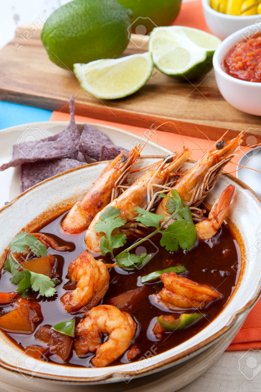 Closeup of a bowl of hot delicious spicy Mexican shrimp soup, garnished with whole shrimps and fresh cilantro. Limes, blue corn chips, salsa, guacamole, and marinated hot pepper. - 165786051 Closeup of a bowl of hot delicious spicy Mexican shrimp soup, garnished with whole shrimps and fresh cilantro. Limes, blue corn chips, salsa, guacamole, and marinated hot pepper. - 165786051