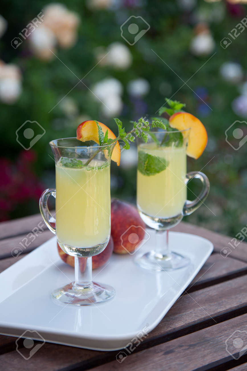 Closeup of Peach Mojito garnished with peach wedge and twig of mint. Outside cocktails / drinks in a garden. - 166616950 Closeup of Peach Mojito garnished with peach wedge and twig of mint. Outside cocktails / drinks in a garden. - 166616950