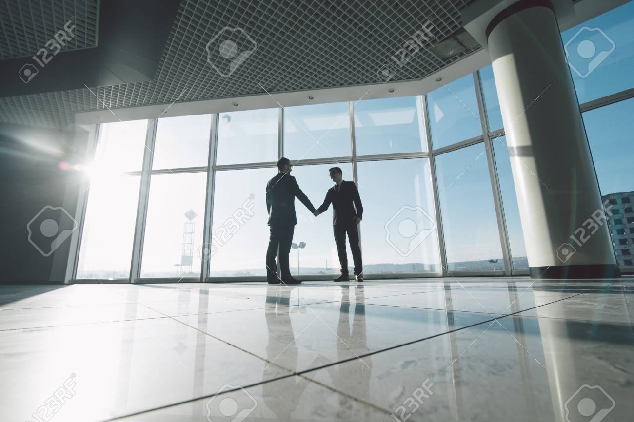 Full Length Side View Of Businessmen Shaking Hands In Against