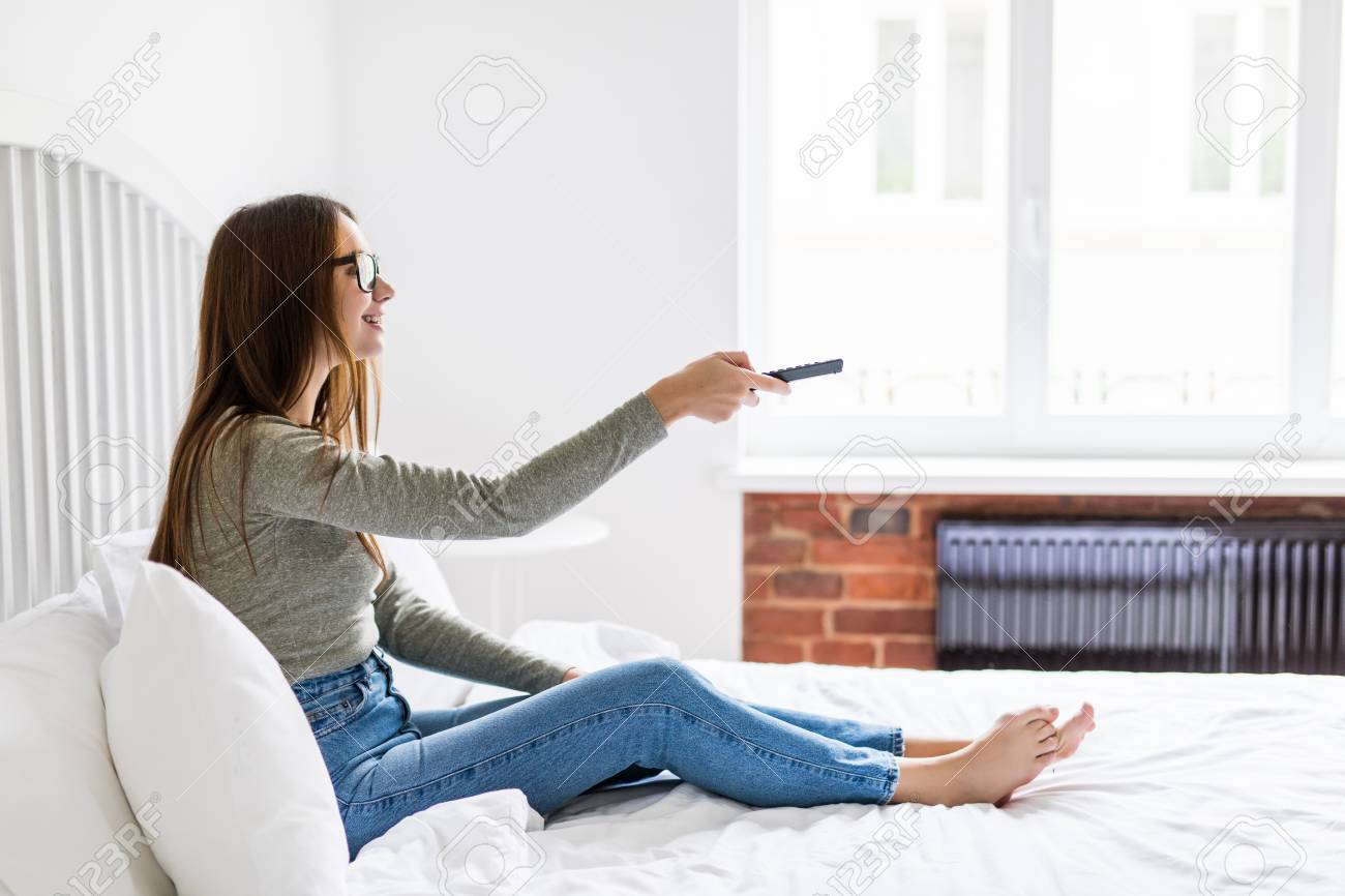 テレビのリモコンを持っている女の子 チャンネルを変更します 一人でテレビを見てリモコンで自宅に座っているセクシーな女性 の写真素材 画像素材 Image