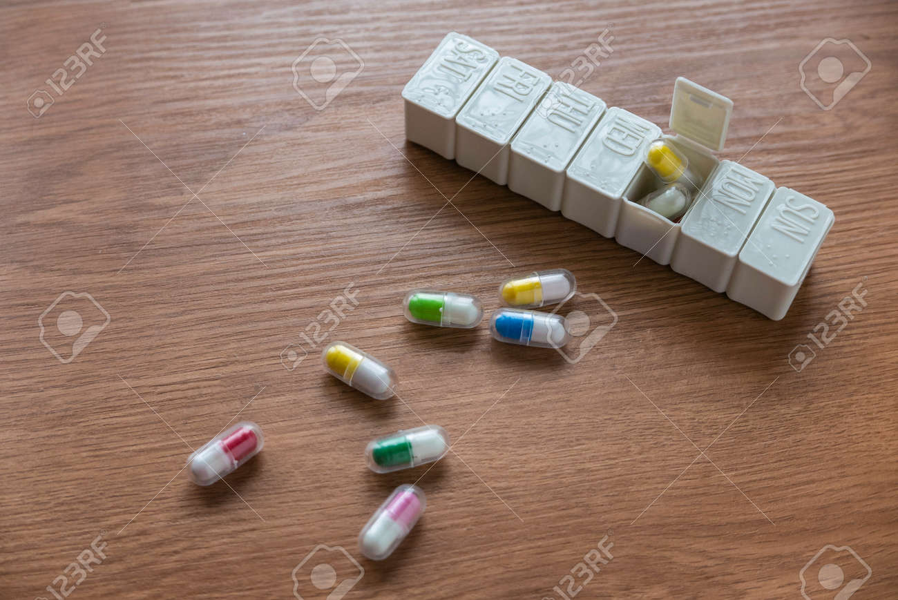 Selective focus of pill box with spilled pills on wooden table. - 169596819 Selective focus of pill box with spilled pills on wooden table. - 169596819