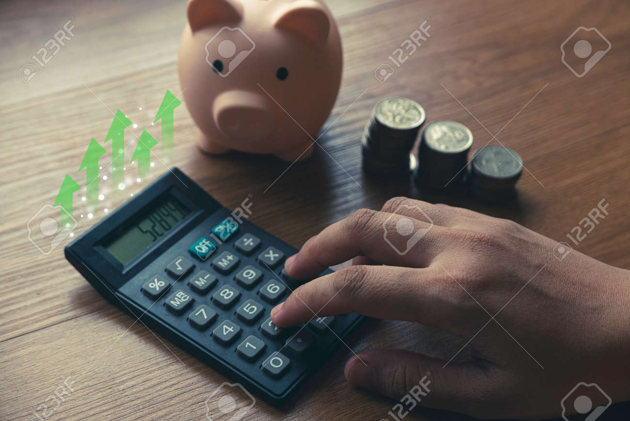 Business and finance concept with hand pressing calculator , a stack of coins and piggy bank. - 169596852 Business and finance concept with hand pressing calculator , a stack of coins and piggy bank. - 169596852
