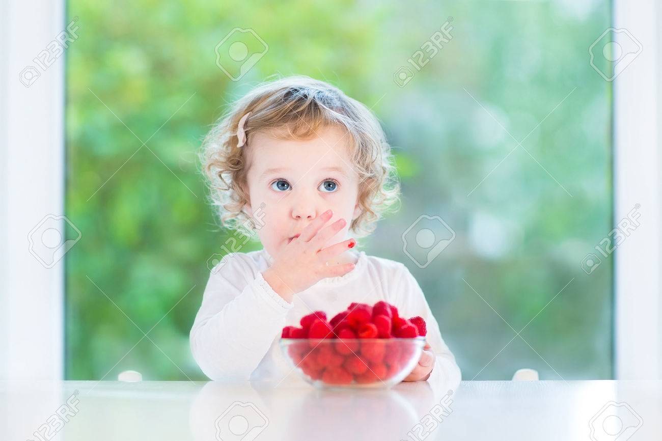 Drole Fille De Bebe Manger Framboise Mignon A Une Table Blanche A Cote D Une Grande Fenetre Banque D Images Et Photos Libres De Droits Image