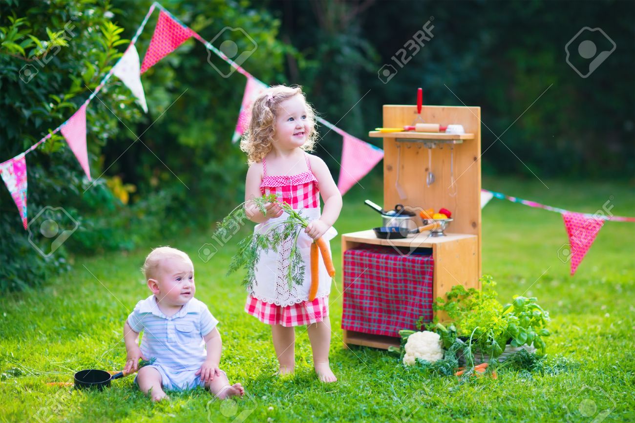 おもちゃのキッチンで遊ぶ子供たち 子供たちは 夏の庭で遊ぶ 男の子と女の子の料理と裏庭で野菜を焼きます 幼児子供や赤ちゃんが一緒に調理します 夏の屋外の楽しみ の写真素材 画像素材 Image