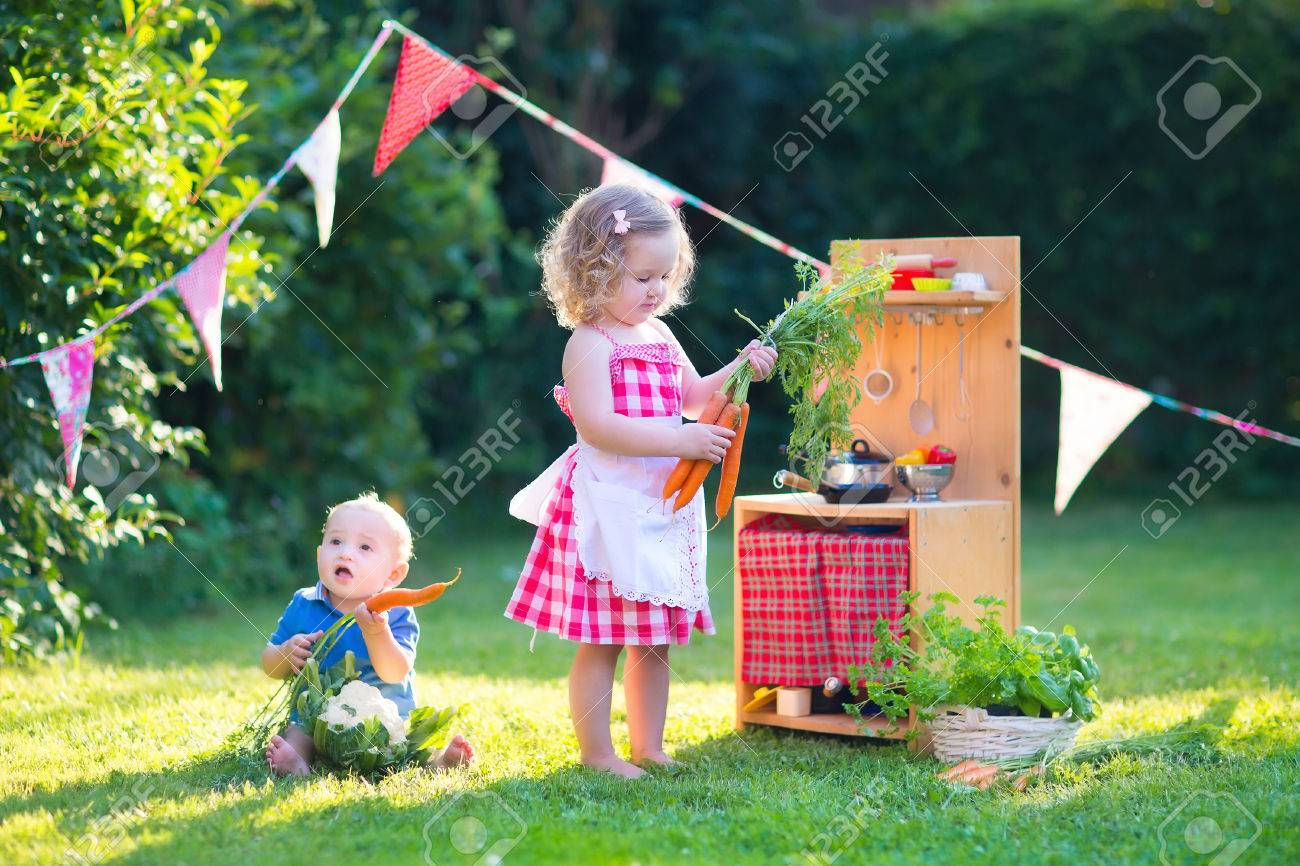 おもちゃのキッチンで遊ぶ子供たち 子供たちは 夏の庭で遊ぶ 男の子と女の子の料理と裏庭で野菜を焼きます 幼児子供や赤ちゃんが一緒に調理します 夏の屋外の楽しみ の写真素材 画像素材 Image