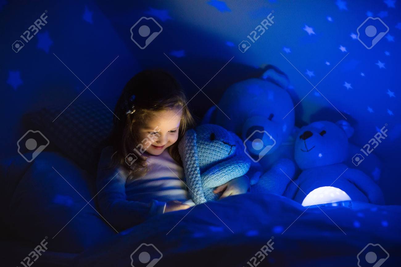 Little Girl Reading A Book In Bed Dark Bedroom With Night Light