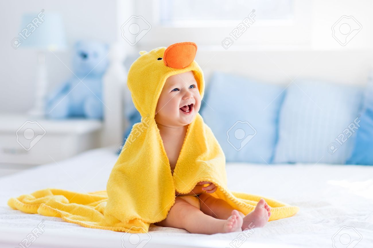 Happy laughing baby wearing yellow hooded duck towel sitting on parents bed after bath or shower. Clean dry child in bedroom. Bathing and washing of little kids. Children hygiene. Textile for infants. - 54640071 Happy laughing baby wearing yellow hooded duck towel sitting on parents bed after bath or shower. Clean dry child in bedroom. Bathing and washing of little kids. Children hygiene. Textile for infants. - 54640071