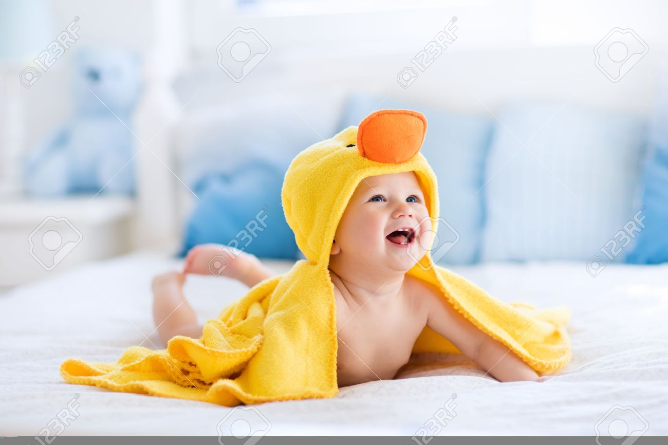 Happy laughing baby wearing yellow hooded duck towel sitting on parents bed after bath or shower. Clean dry child in bedroom. Bathing and washing of little kids. Children hygiene. Textile for infants. - 55198432 Happy laughing baby wearing yellow hooded duck towel sitting on parents bed after bath or shower. Clean dry child in bedroom. Bathing and washing of little kids. Children hygiene. Textile for infants. - 55198432