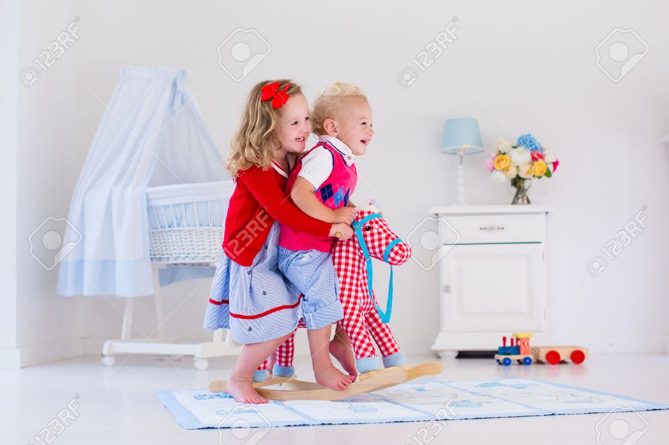 2 人 の子供は室内で遊ぶ 子供おもちゃロッキング馬に乗って 男の子と女の子のデイケアや幼稚園で遊んで 赤ちゃんと幼児のための美しい保育園 幼児のためのおもちゃ 兄と妹の 家で の写真素材 画像素材 Image