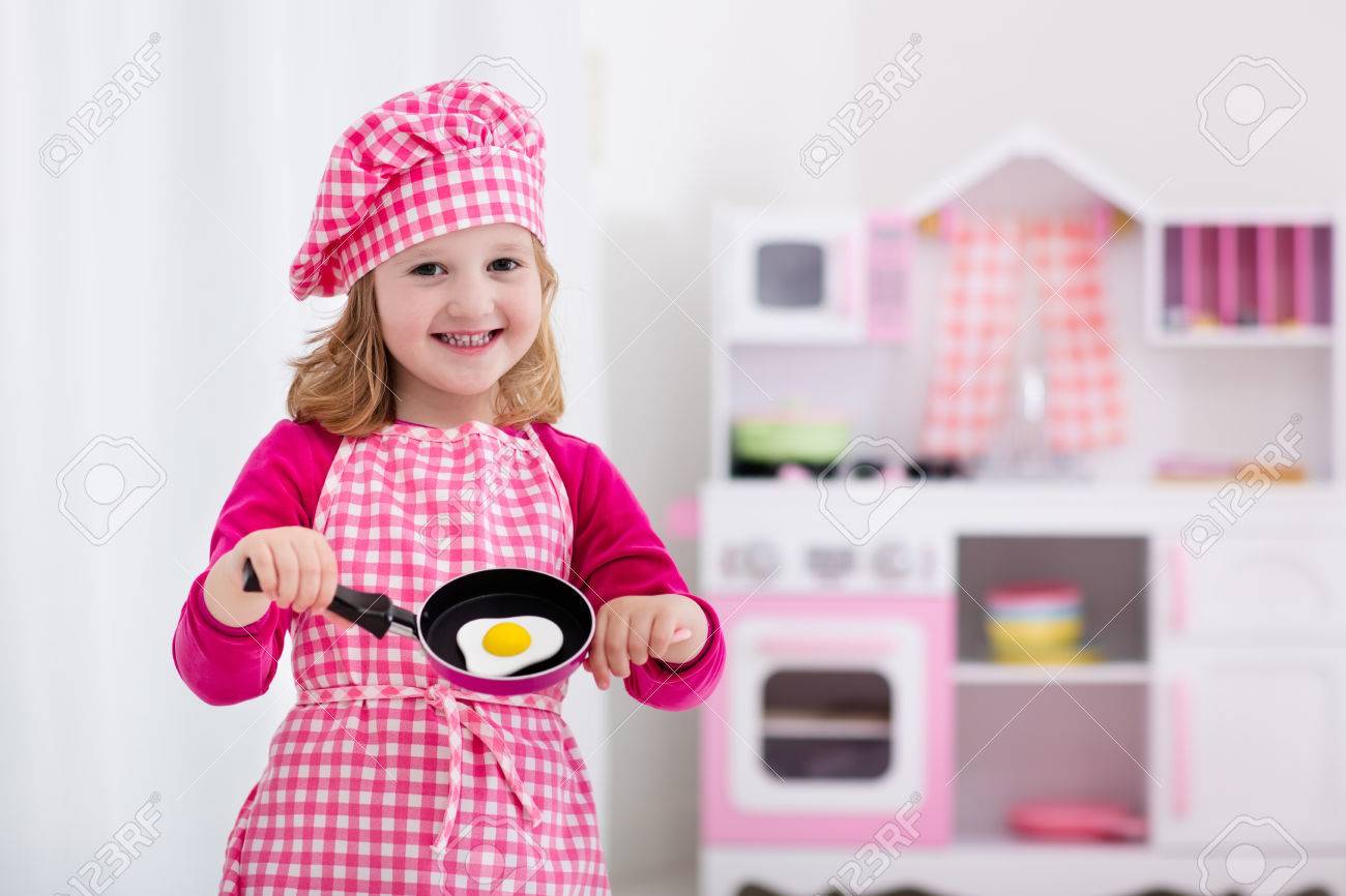 Little Girl In Chef Hat And Apron Cooking Fried Eggs In Toy