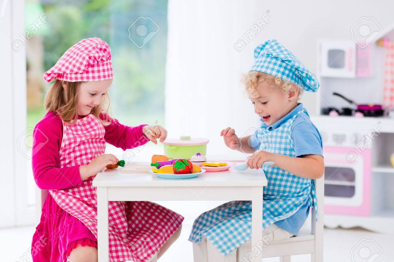 Little Girl And Boy In Chef Hat And Apron Cooking In Toy Kitchen