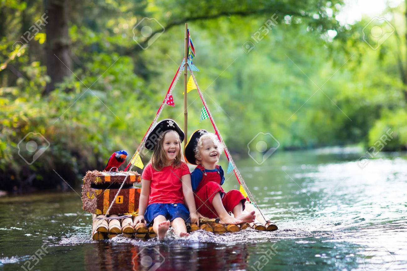 子供たちは海賊の衣装や宝箱 Spyglasses 暑い夏の日に川でセーリング木製いかだに乗って遊んで剣と帽子に身を包んだ 海賊の役割は子供のためのゲーム 楽しい家族のための水します の写真素材 画像素材 Image