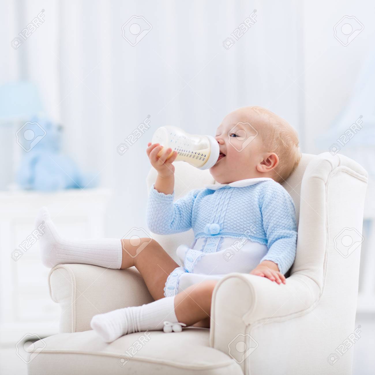 Adorable Baby Boy Playing On A Blue Floor Mat And Drinking Milk