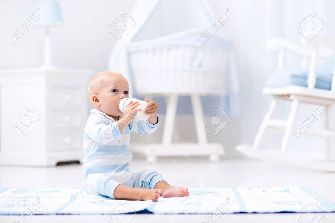 Adorable Baby Boy Playing On A Blue Floor Mat And Drinking Milk