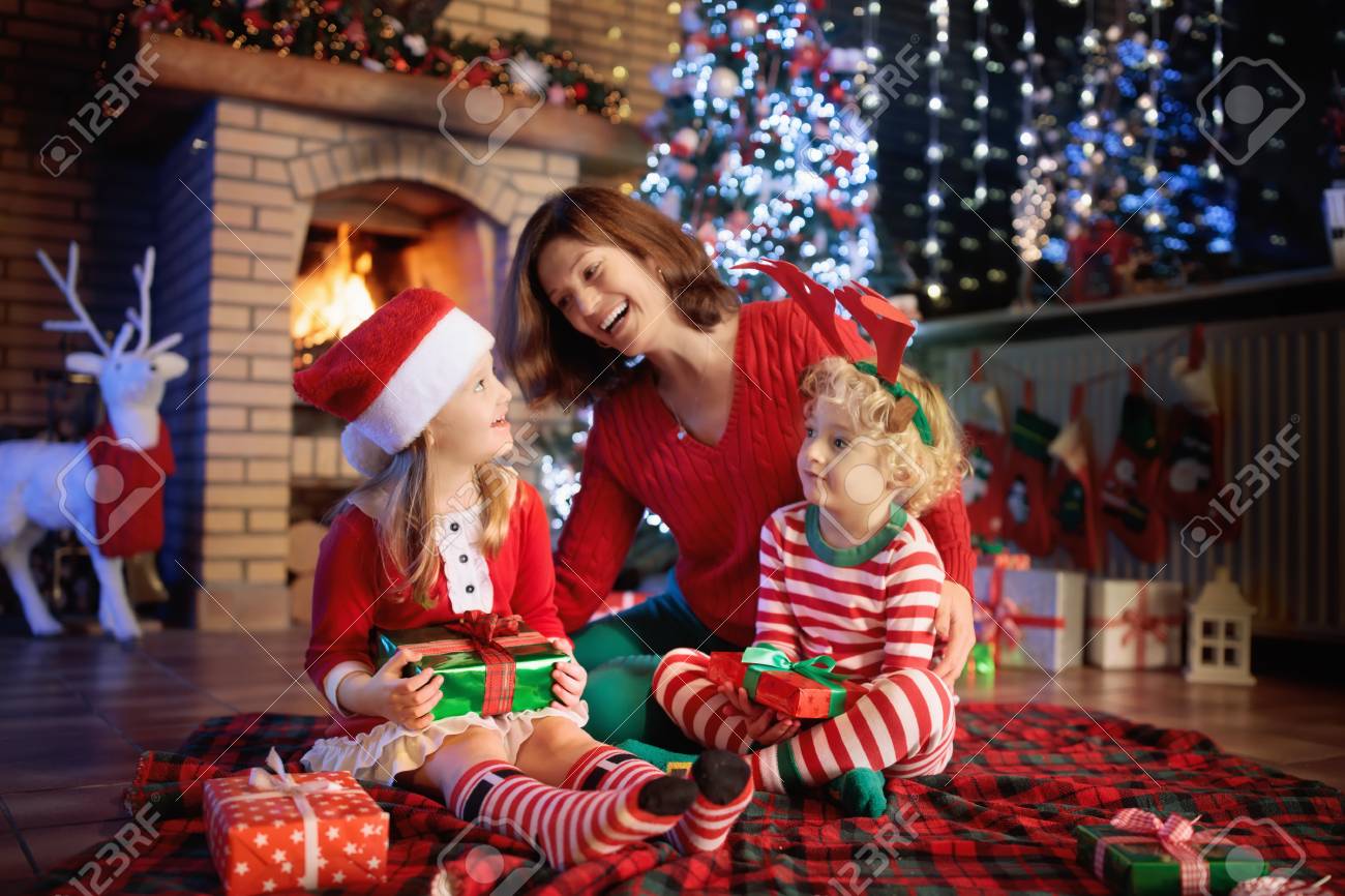 クリスマス ツリーと暖炉で子供を持つ家族 母と子の火の場所でプレゼントを開きます 少年は 少女とお母さんはプレゼントが開きます 冬の休日の室内装飾 クリスマス イヴにパジャマの子 の写真素材 画像素材 Image 08