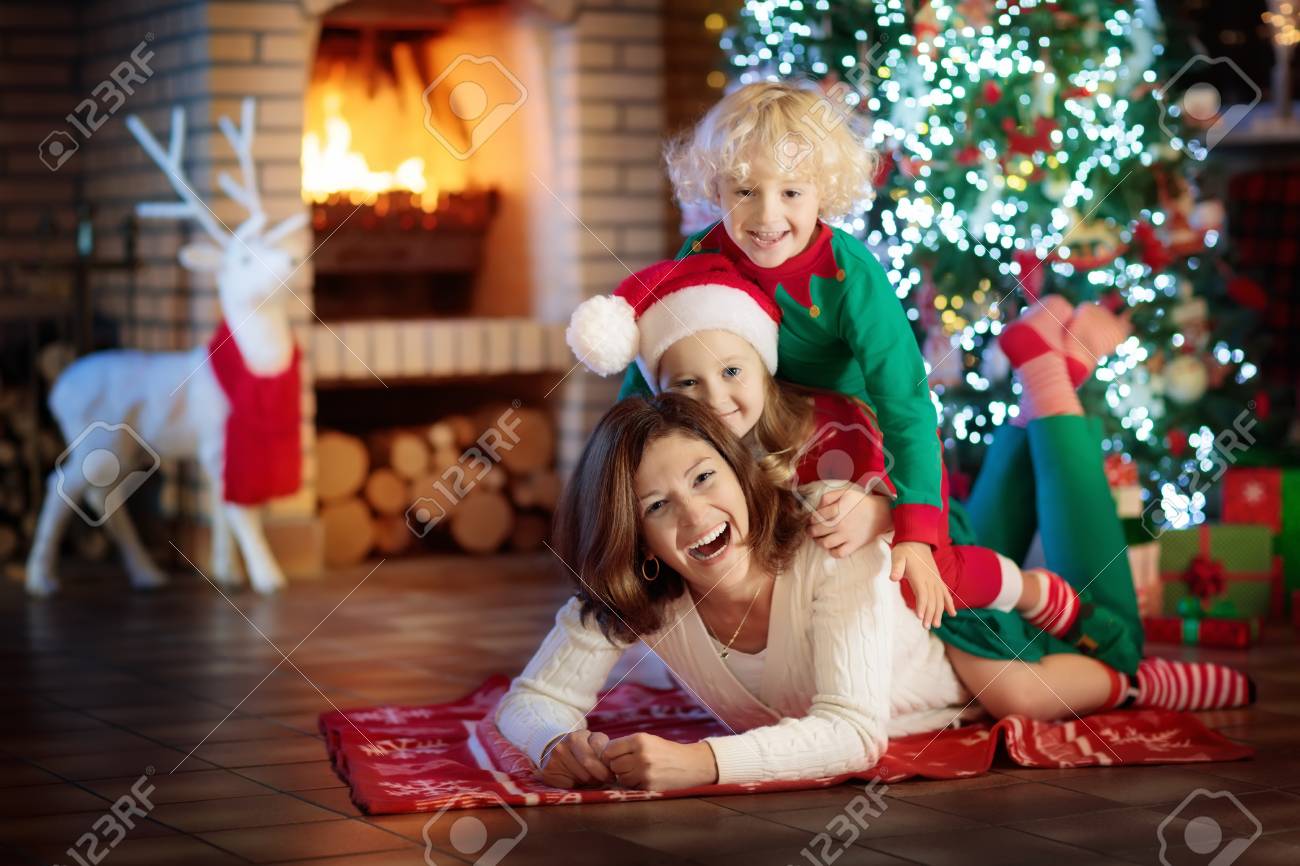 クリスマス ツリーと暖炉で子供を持つ家族 母と子の火の場所でプレゼントを開きます 少年は 少女とお母さんはプレゼントが開きます 冬の休日の室内装飾 クリスマス イヴにパジャマの子 の写真素材 画像素材 Image
