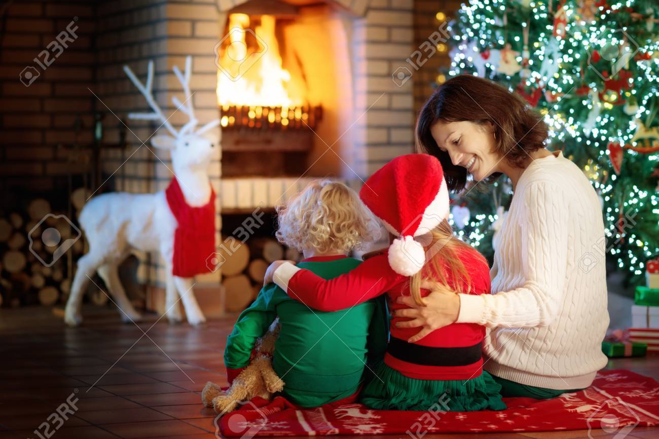 クリスマス ツリーと暖炉で子供を持つ家族 母と子の火の場所でプレゼントを開きます 少年は 少女とお母さんはプレゼントが開きます 冬の休日の室内装飾 クリスマス イヴにパジャマの子 の写真素材 画像素材 Image