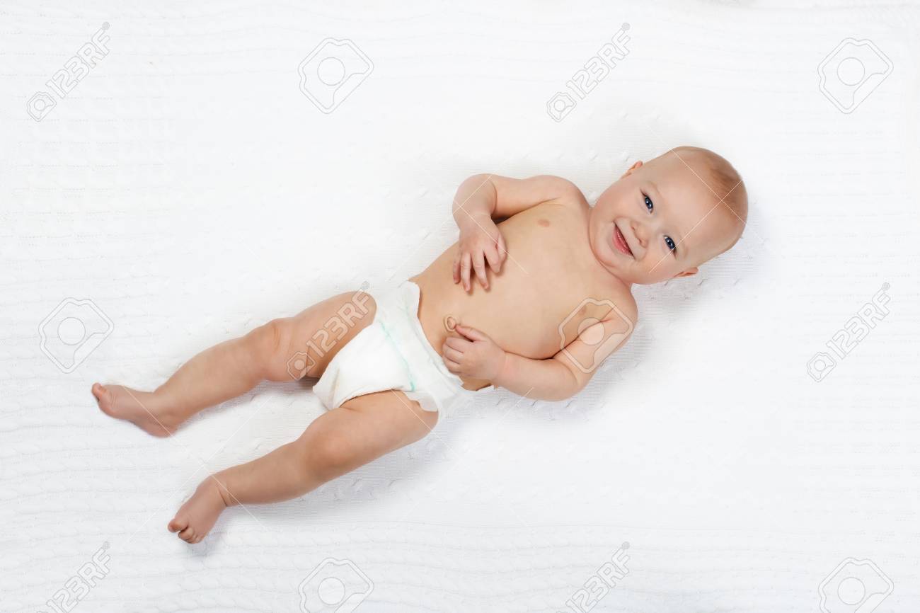 Funny little baby wearing a diaper playing on a white knitted blanket in a sunny nursery. Child after bath or shower on a fresh towel. Infant nappy change and skin care. Cute kid playing with his feet - 102165199 Funny little baby wearing a diaper playing on a white knitted blanket in a sunny nursery. Child after bath or shower on a fresh towel. Infant nappy change and skin care. Cute kid playing with his feet - 102165199